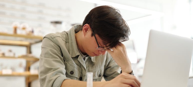 Tired man looking at his laptop and worrying about can you get fired for going to rehab.