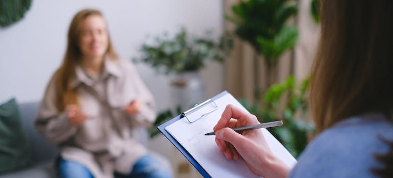 Woman writing in a clipboard while talking to a patient.