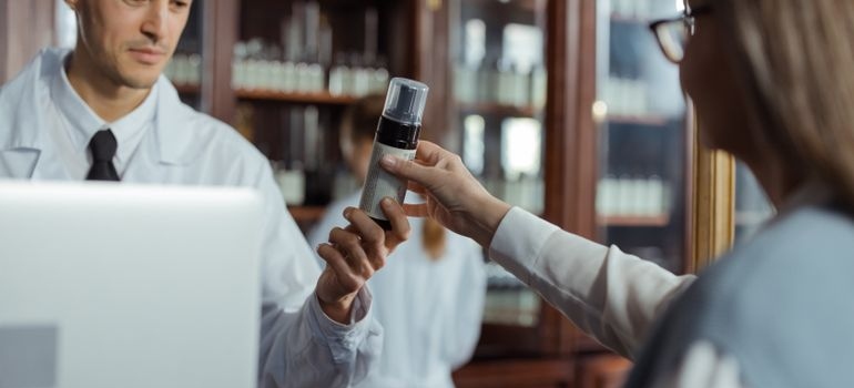 Pharmacist handing a medication bottle to a customer across a pharmacy counter.