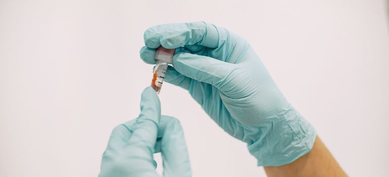 Laboratory worker wearing protective gloves holding a test tube containing a sample.