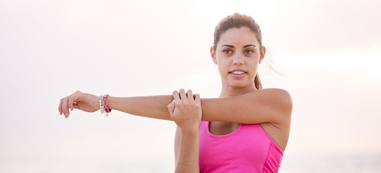 Woman in a pink top stretching her upper body before a run.