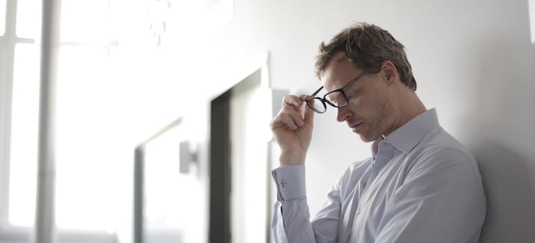 Man leaning against the wall and taking off his glasses.