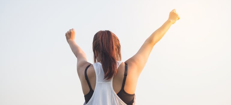 Woman in a tank top lifting her hands toward the sky.