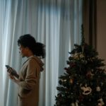 Woman standing next to a Christmas tree and looking out of the window.