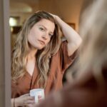 Woman holding a mug and looking at herself in the mirror.