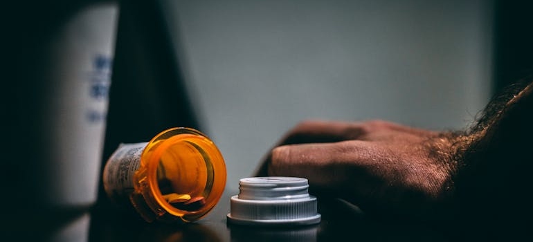 Man's hand next to an empty pill bottle.