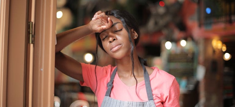 Caffee worker leaning against the door while struggling with ongoing fatigue.