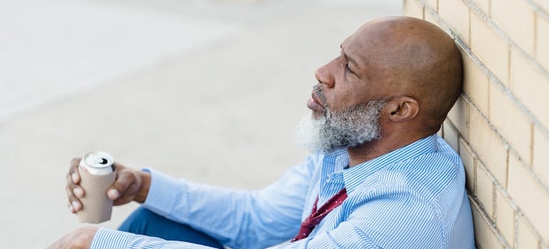 Man leaning against a wall while drinking a can of beer.