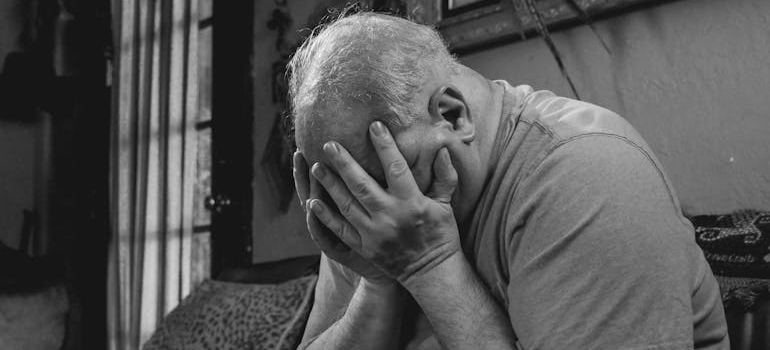 Older man sitting on the couch and crying with his face in his hands.