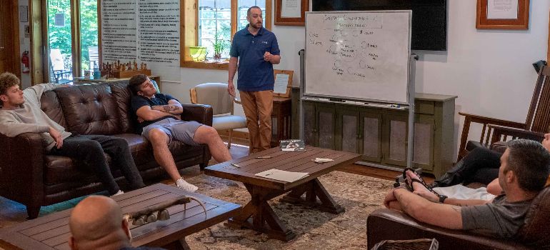 A therapy session at little creek - a therapist is standing in front of the white board and the patients are sitting on the couches around him