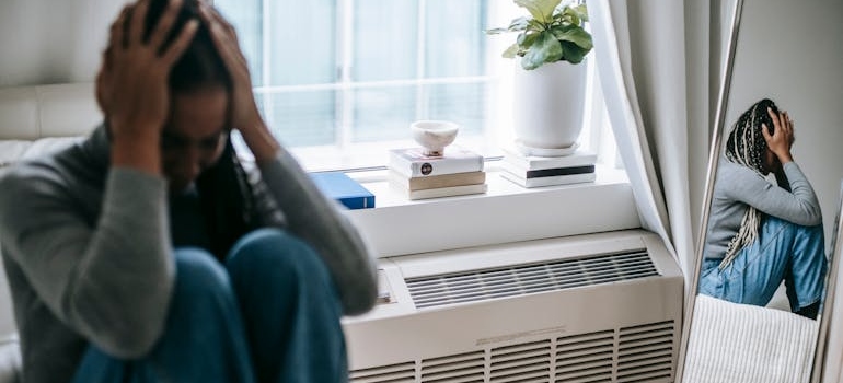 Woman sitting on the bed and covering her head with her hands.