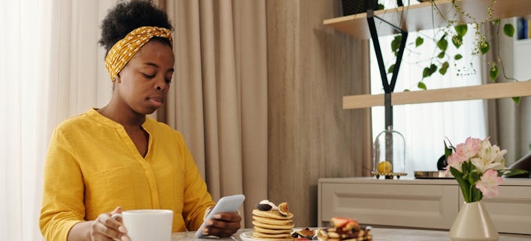 Woman looking at her phone while drinking coffee and eating breakfast.