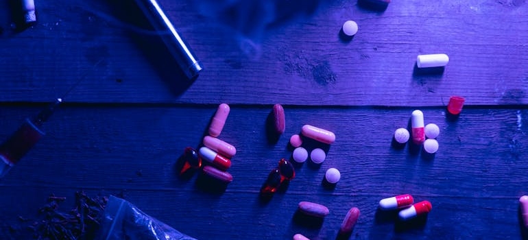 Pills, marijuana and a syringe on a wooden table.