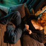 Woman sitting on the bed surrounded by beer bottles and pills after mixing alcohol with drugs.