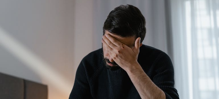 Man sitting on the bed and rubbing his forehead with his hand.