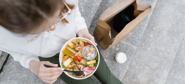 Woman sitting on the stairs and eating a salad.