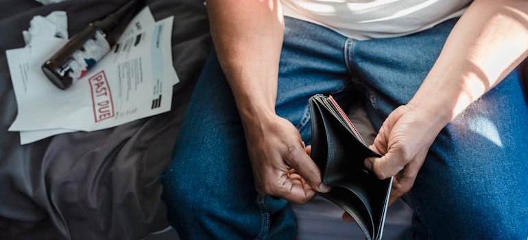 Man opening an empty wallet with bills and beer bottles next to him.