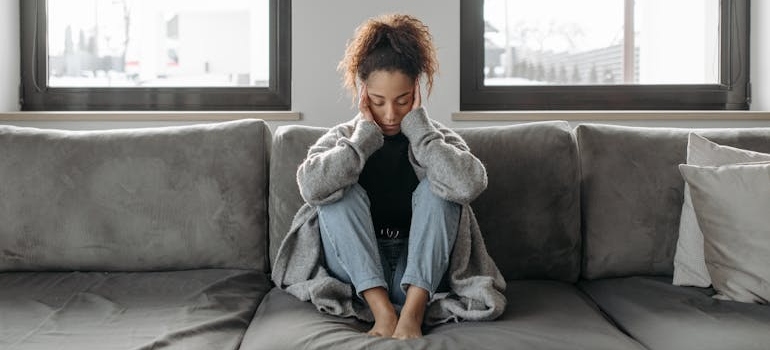 Woman with a headache sitting on the couch and holding her head.