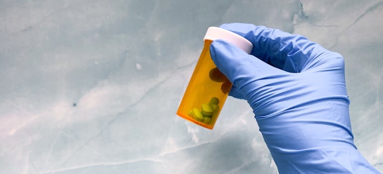 Nurse holding an orange bottle of blue pills.