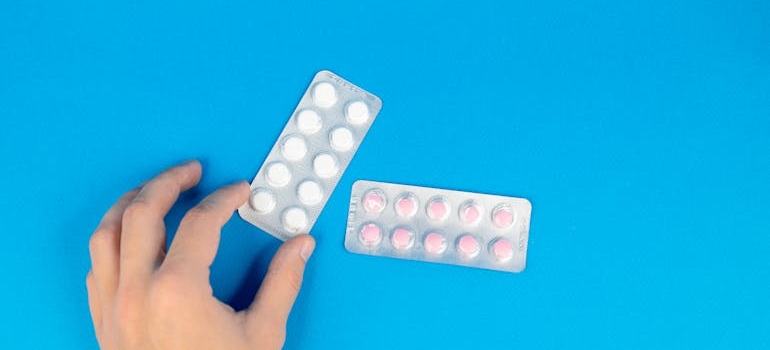 Two blisters of pills on a blue background and a hand picking up one of them.