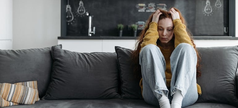 Woman sitting on the couch and worrying about her issues with people-pleasing and addiction.