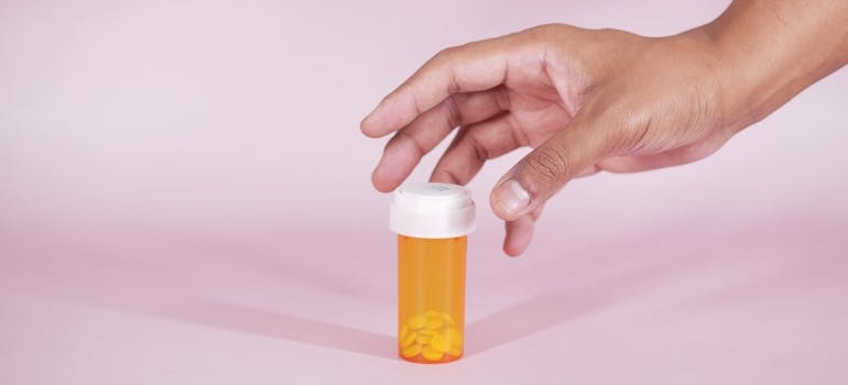 Person grabbing an orange bottle of prescription pills.