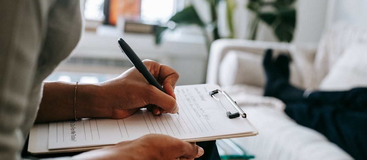 Therapist writing in a clipboard while talking with a patient about their social life after rehab.