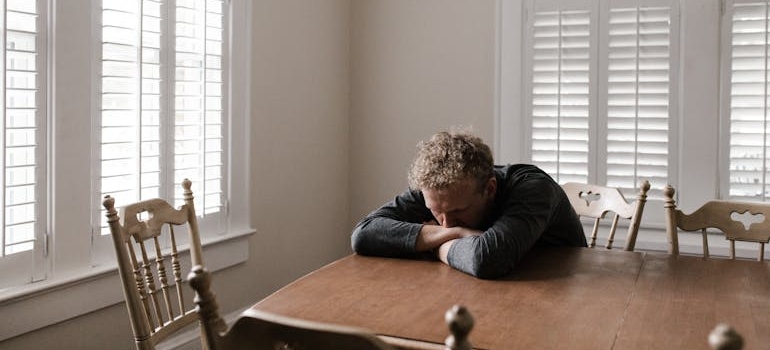 Man sitting at the table with his head in his arms.