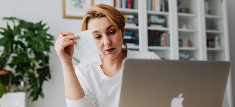 Woman looking at her laptop while holding a bill.
