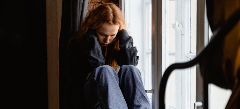 Woman sitting next to her window and covering her ears.