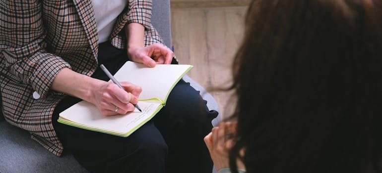 Therapist writing in a notebook while listening to a client.