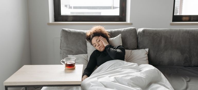 Woman lying on the couch and rubbing her head.