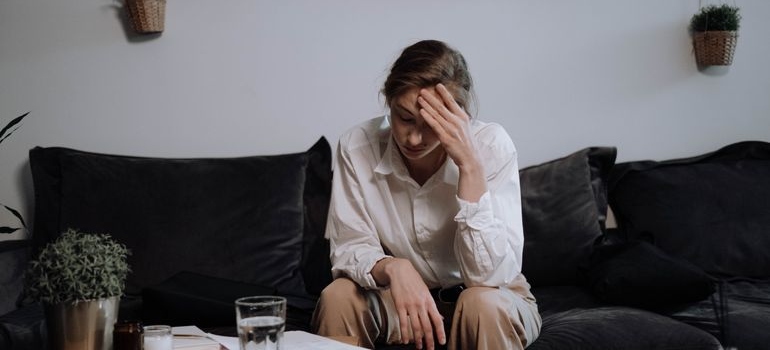 Woman sitting on the couch and worrying about the impact of hormones on substance use disorders.