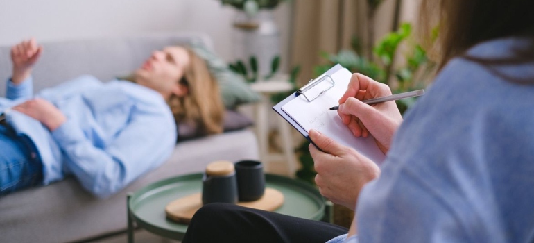 Therapist writing in a clipboard while talking with a patient about performance pressure and substance use.