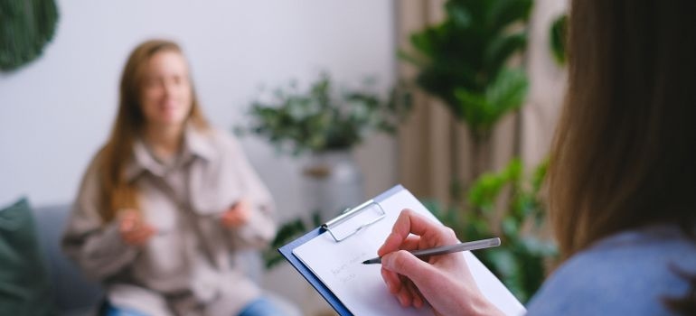 Therapist writing in a clipboard while talking with a client.
